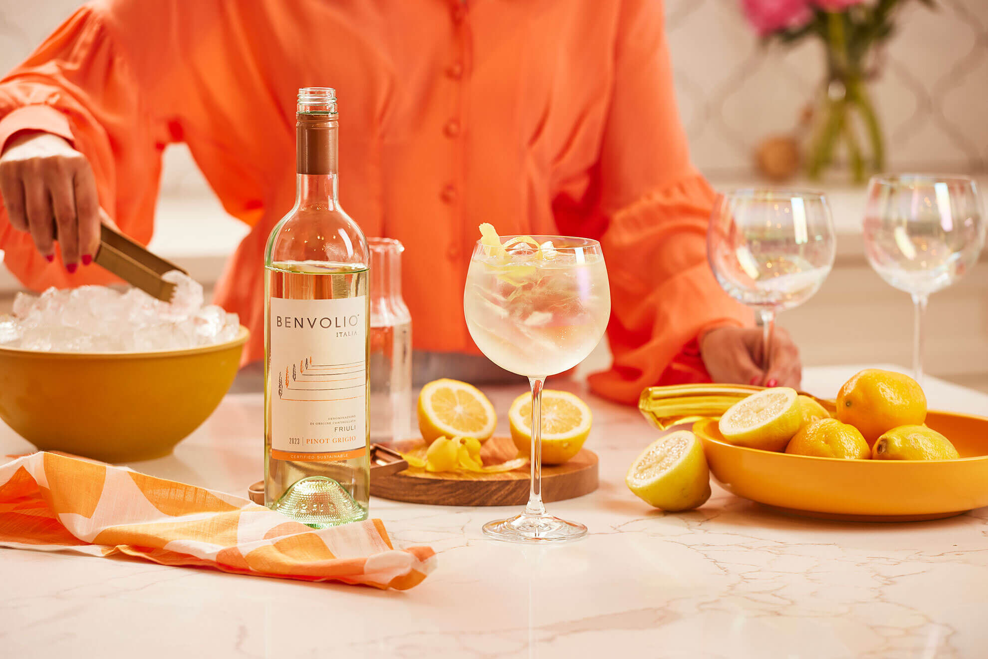 Benvolio Pinot Grigio on marble counter with a person in orange shirt adding ice for a cocktail